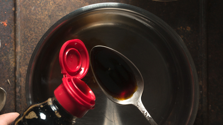 pouring soy sauce into a teaspoon over a saucepan