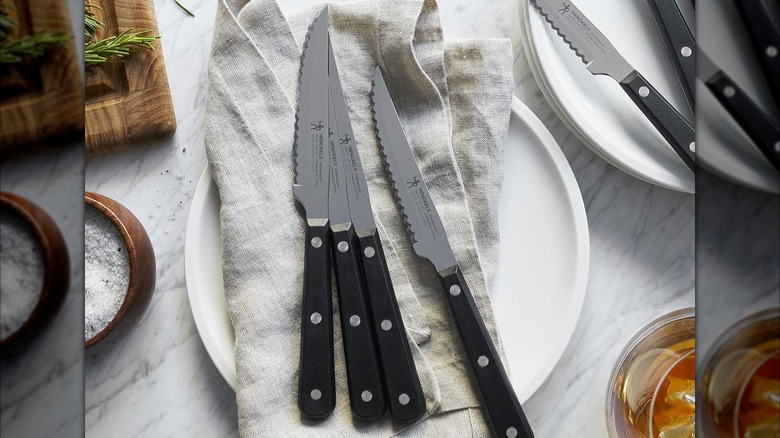 Four Henckels steak knives on dinner plates and napkins