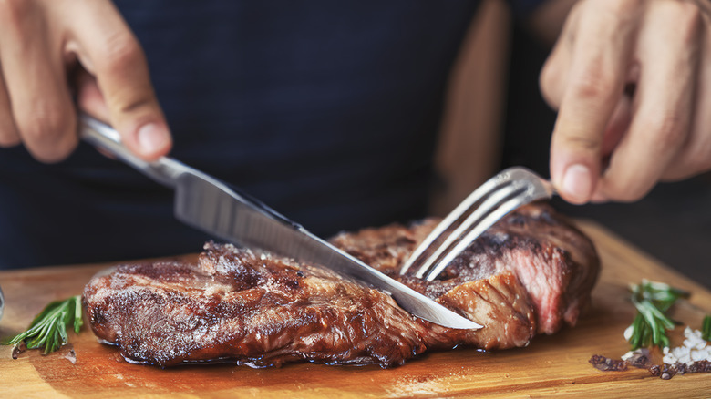 Person cutting piece of steak on wooden board