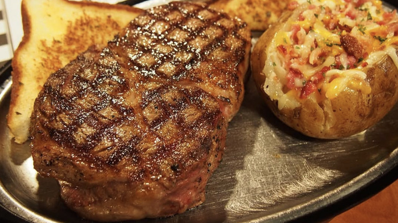 Steak, baked potato and bread on plate