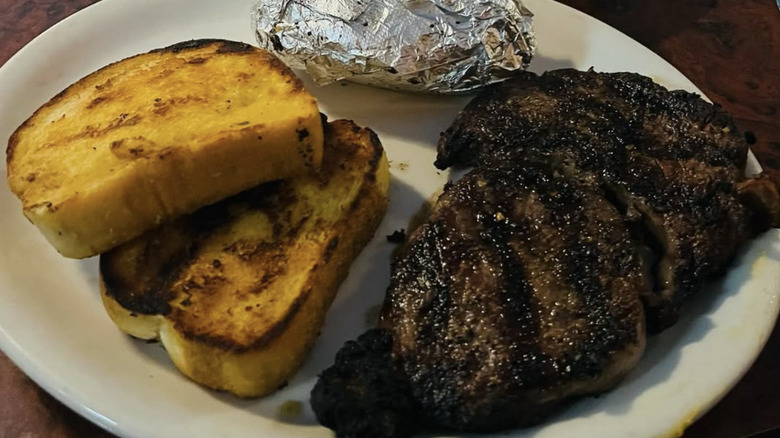 Steak, garlic bread, and wrapped baked potato on plate