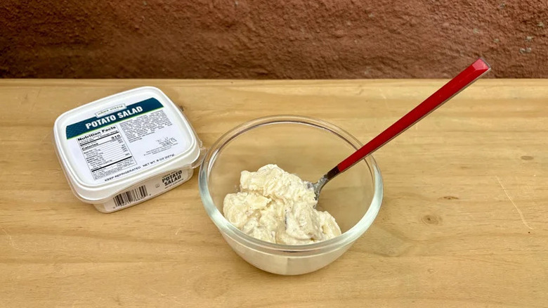 A container of Häns Kissle potato salad beside a glass bowl filled with it and a red spoon