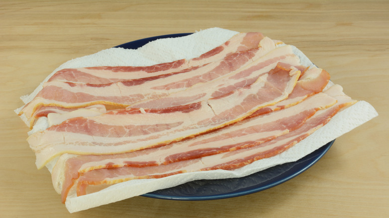 Raw bacon strips on a paper towel-lined plate