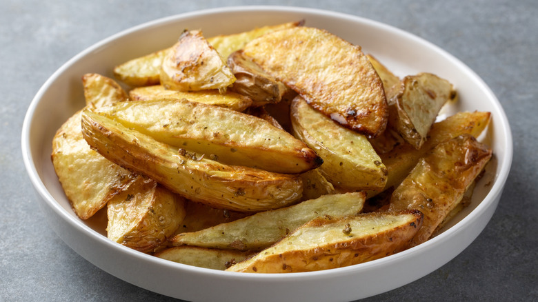 Crispy seasoned potato wedges in a white bowl
