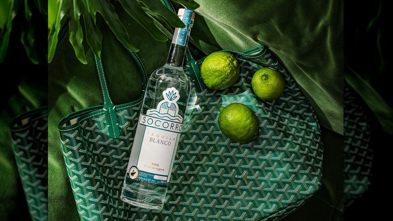 A bottle of Socorro blanco with limes and a tote bag