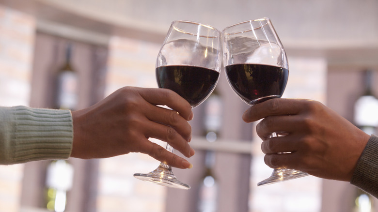 two people holding red wine in glass