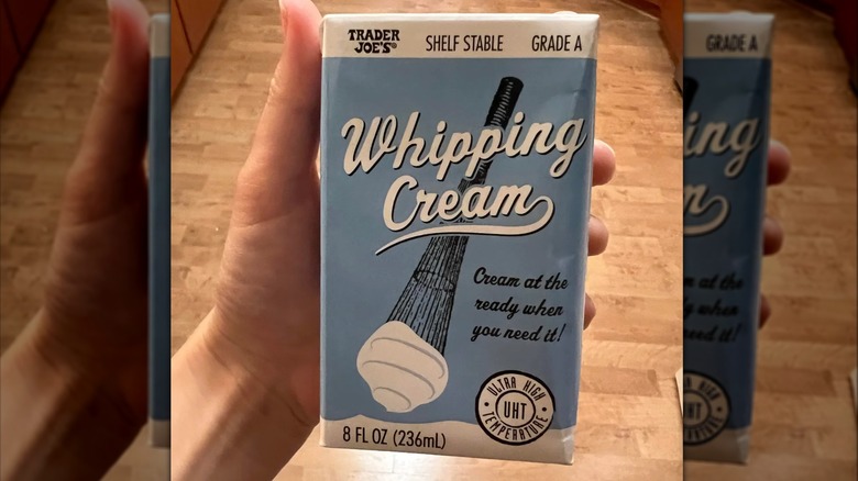A hand holds a box of Trader Joe's shelf stable whipping cream.