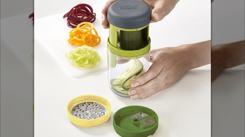 A person cutting a zucchini with a Joseph Joseph hand-held spiralizer