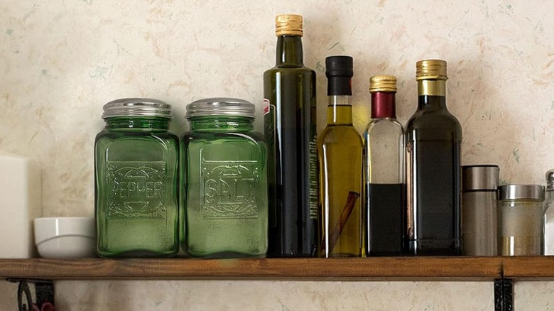 Depression glass style salt and pepper shakers on a shelf with other bottles
