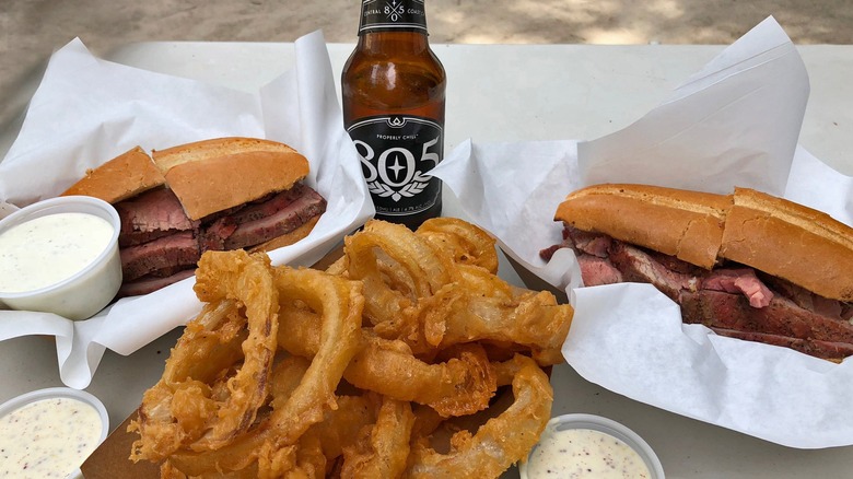 Two tri-tip sandwiches with onion rings and a beer