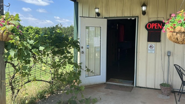 Door to the Native Spirits Winery tasting room open, with red open sign, hanging flowers and grapevines trailing over a fence outside.