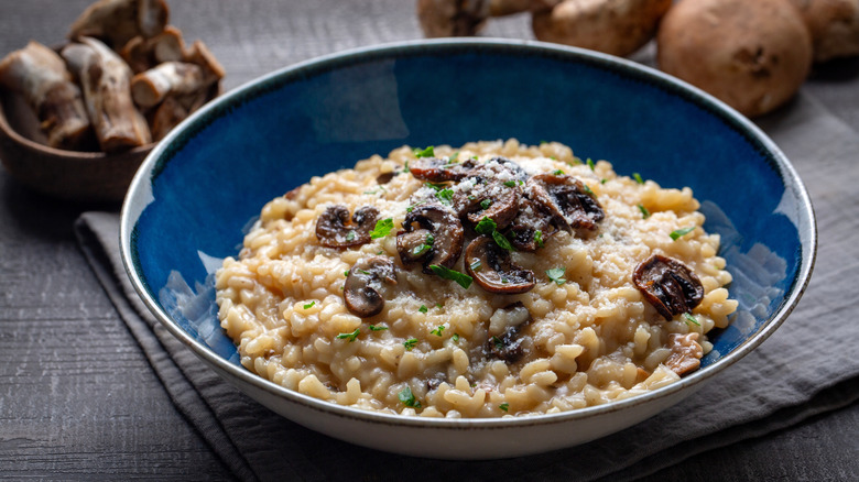 mushroom risotto in blue bowl on wooden table with mushrooms in background