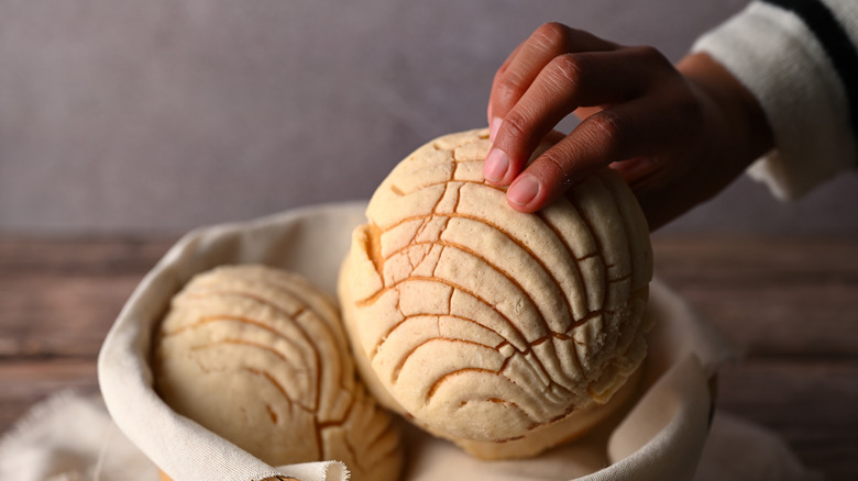 Woman picking up concha bread from basket