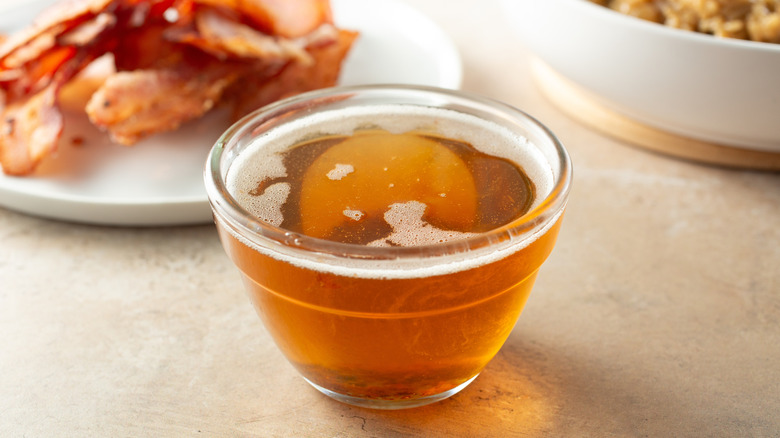 Bacon grease in a small glass bowl next to a plate of bacon