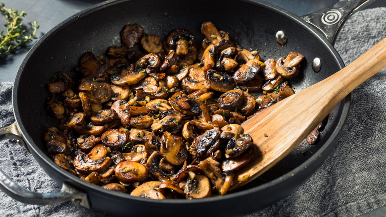 Sauteed sliced mushrooms in skillet with wooden spoon