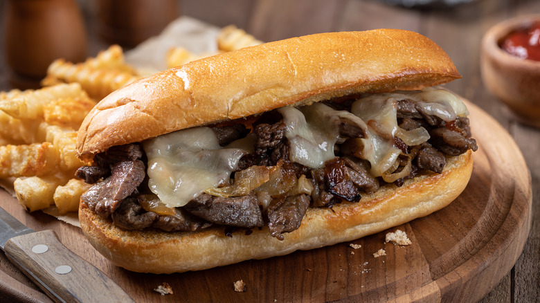 Philly cheesesteak on wooden board with fries