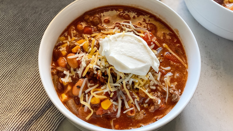 A white bowl of venison chili with cheese and sour cream, made according to Tasting Table's recipe