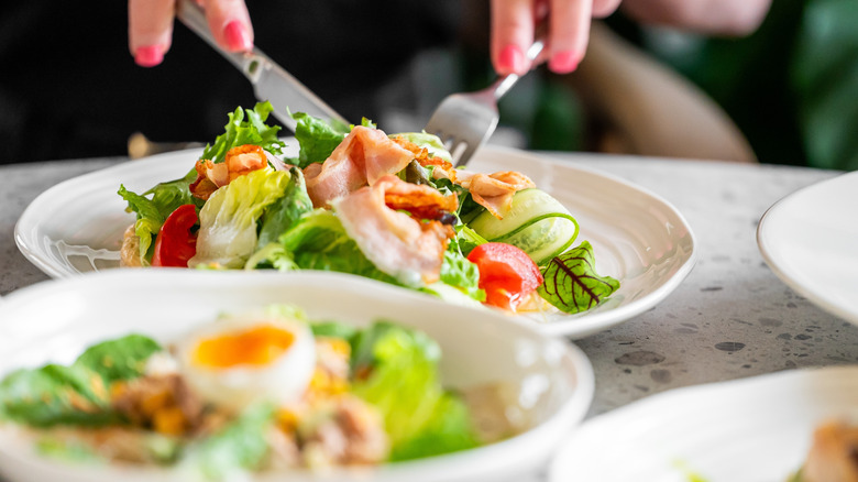 someone slicing into salad with bacon, egg, and tomato