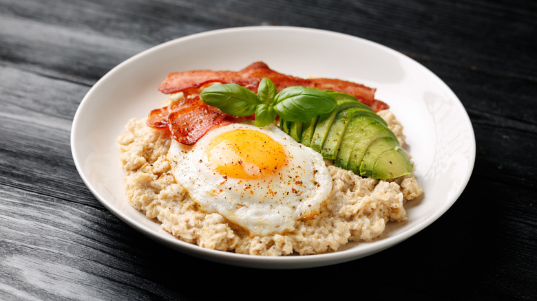 Savory oatmeal bowl with fried egg, avocado, bacon, and fresh basil