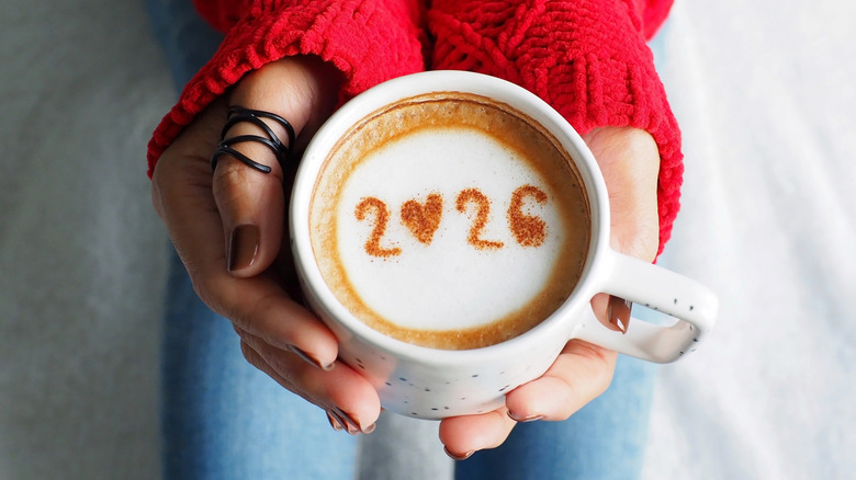 Hand holding coffee mug with 2026 written in the coffee.