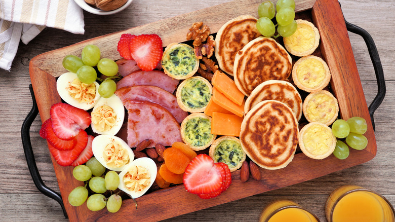 Breakfast grazing charcuterie board with fruit, meat, deviled eggs, mini quiches, nuts, cheese, and mini pancakes