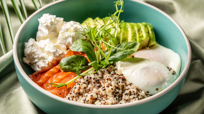 Bowl with cottage cheese, avocado, poached egg, quinoa, smoked salmon, and herbs
