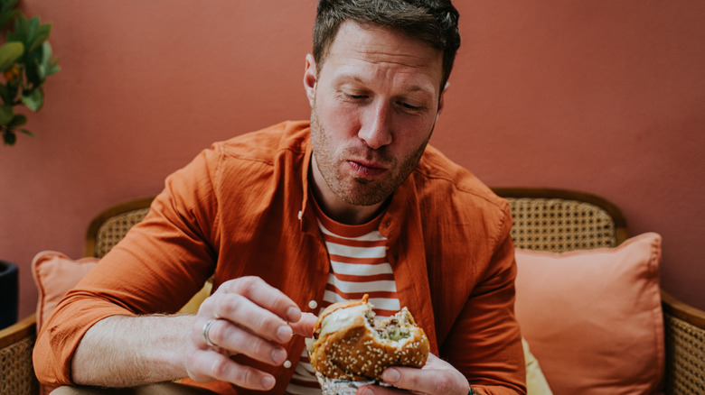 Guy chewing a burger sitting in an orange room