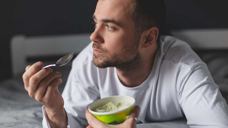 Guy thoughtfully eating a pint of ice cream