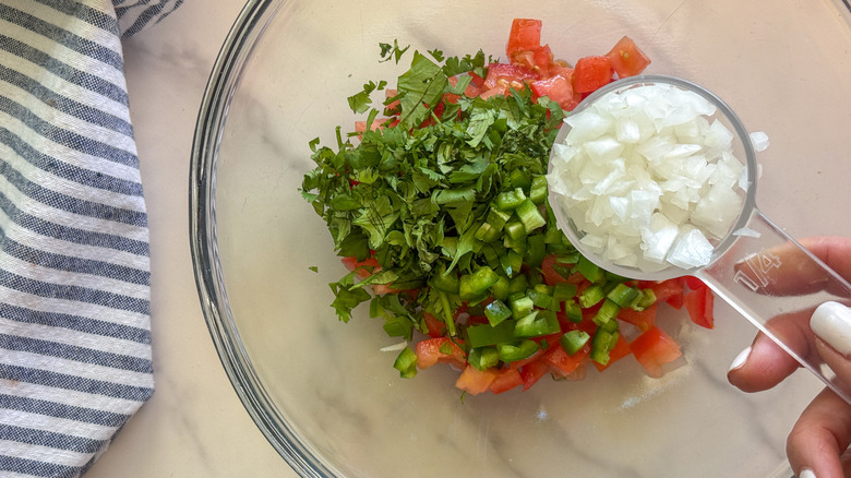 hand adding onion to bowl with pico de gallo ingredients