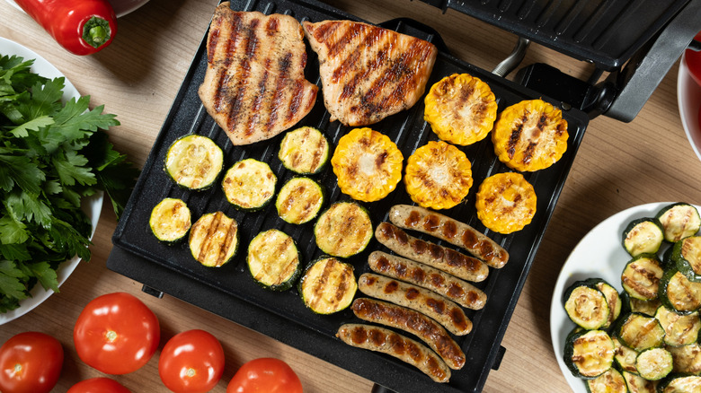 Top view of meat and vegetables cooking on an electric griddle