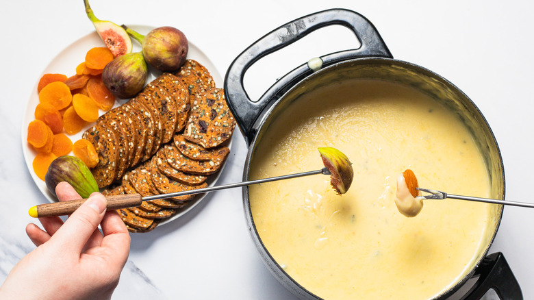 Hand dipping a fresh fig into bleu cheese and honey fondue.
