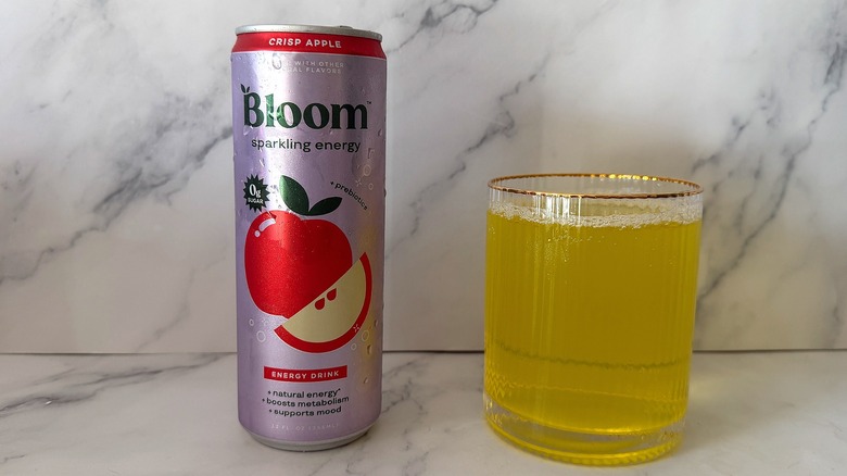 Can of Crisp Apple Bloom Sparkling Energy next to a glass filled with the drink on a marble surface
