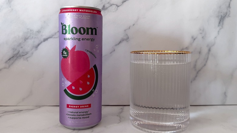 Can of Strawberry Watermelon Bloom Sparkling Energy next to a glass filled with the drink on a marble surface