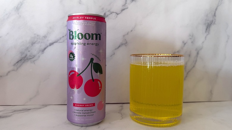 Can of Shirley Temple Bloom Sparkling Energy next to a glass filled with the drink on a marble surface