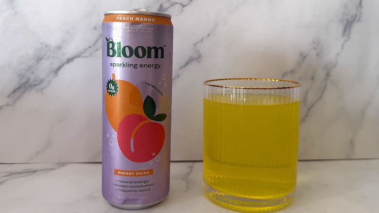 Can of Peach Mango Bloom Sparkling Energy next to a glass filled with the drink on a marble surface