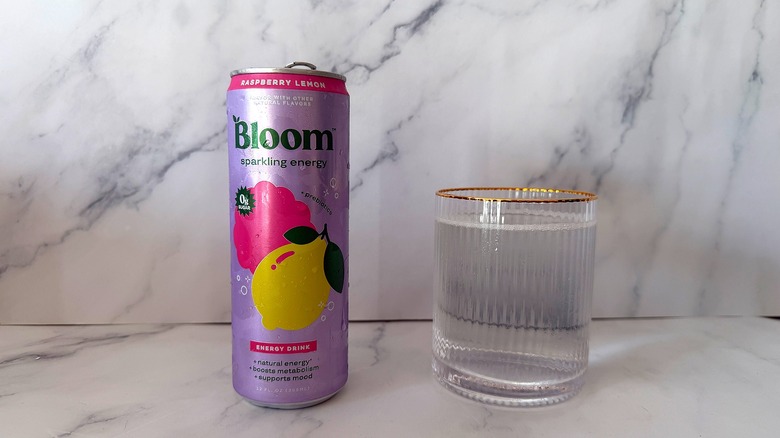 Can of Raspberry Lemon Bloom Sparkling Energy next to a glass filled with the drink on a marble surface