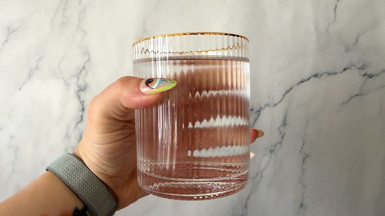 Hand holding a gold-rimmed glass filled with a clear Bloom energy drink
