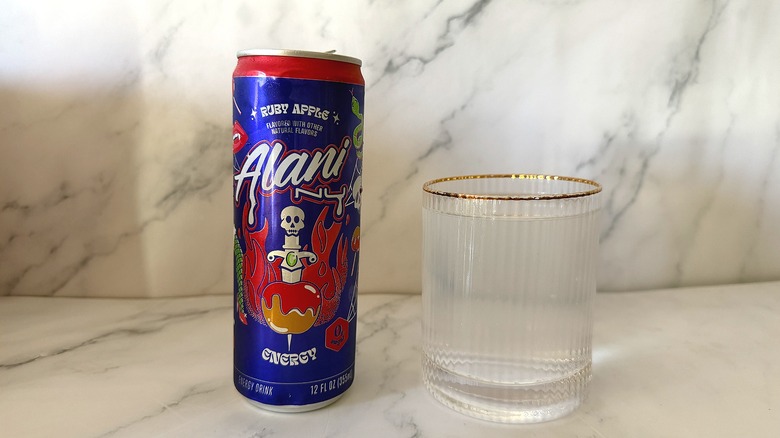 Can of Alani Nu Ruby Apple next to glass of energy drink on marble surface