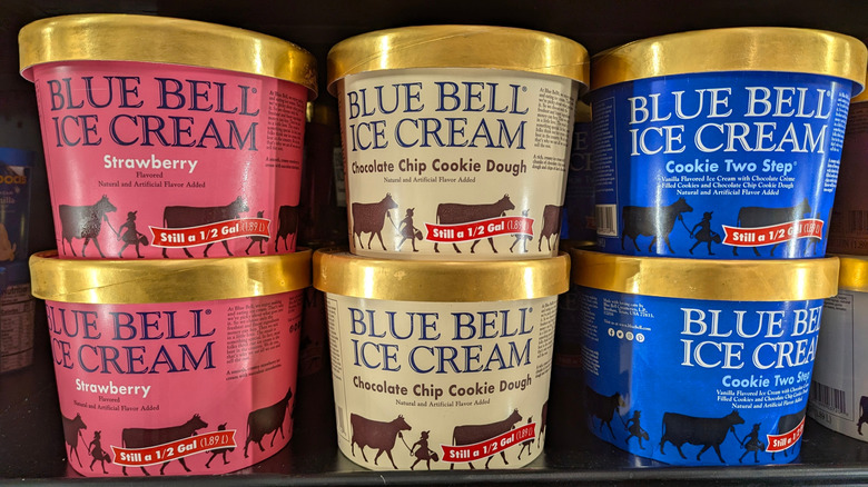 Stacked red, beige, and blue tubs of Blue Bell ice cream in strawberry, cookie dough, and Cookie Two Step flavors