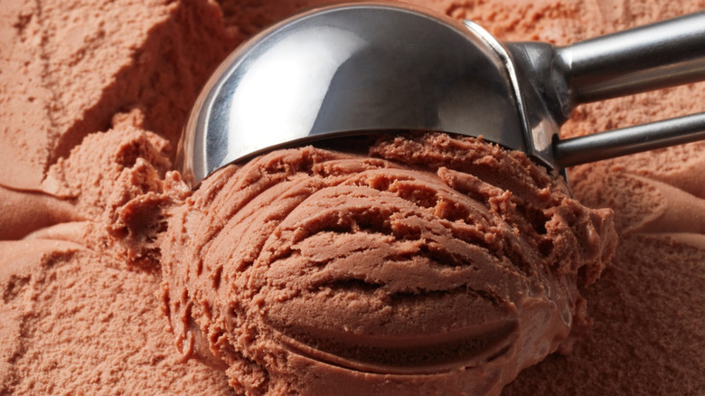 Metal ice cream scoop scooping chocolate ice cream from the container