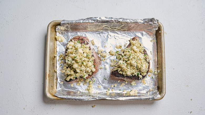 topping steaks with cheese in a sheet pan