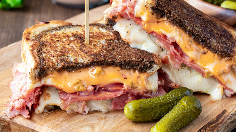 toasted reuben sandwich halves over a wood cutting board with cornichons