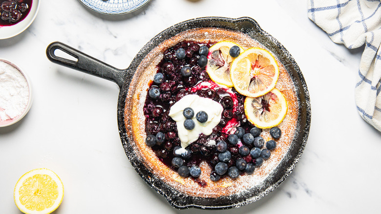 Blueberry lemon dutch baby pancake in cast iron pan with all the toppings around.