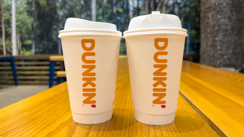 Two Dunkin' hot beverage to-go cups on a wooden table