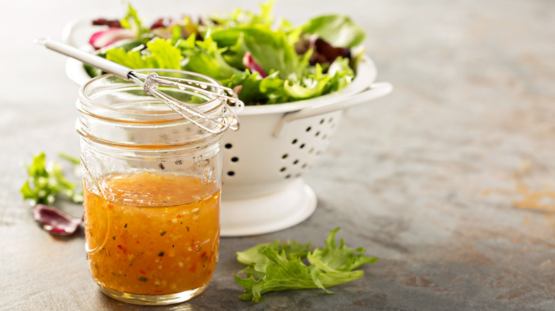 Closeup of vinaigrette and colander of salad greens