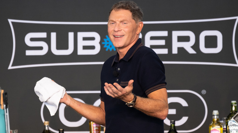 Bobby Flay shrugging during a cooking demo holding a white towel.