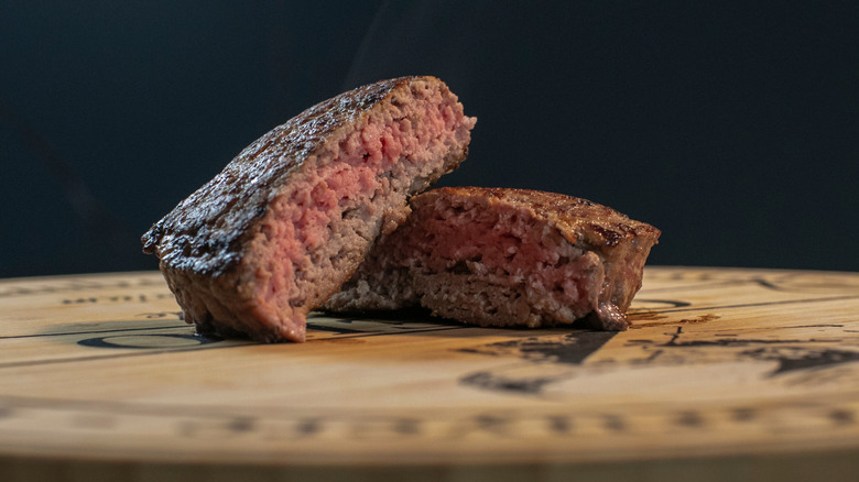 Close-up image of a burger patty cooked medium, sliced in half, and served on a wooden surface