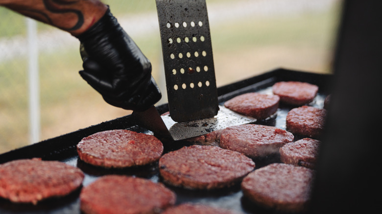 Person pressing a burger patty on a grill using a flat metal spatula