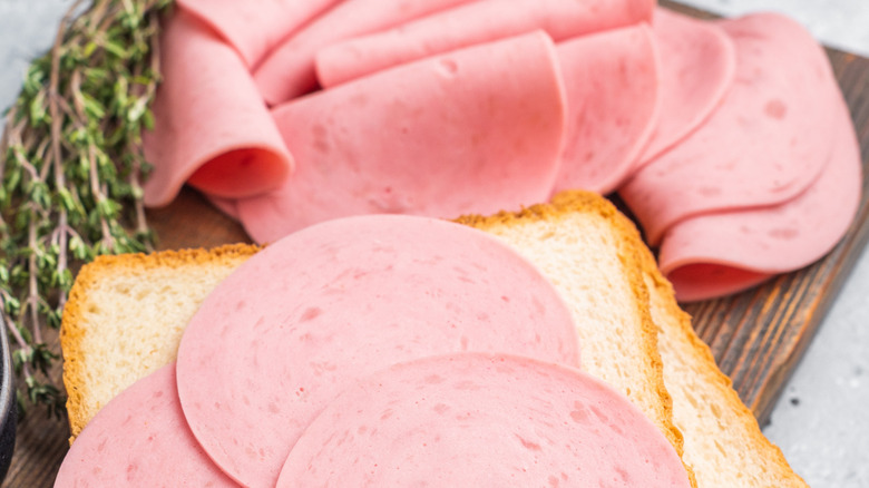 Several slices of bologna on two slices of white bread, with more bologna resting nearby