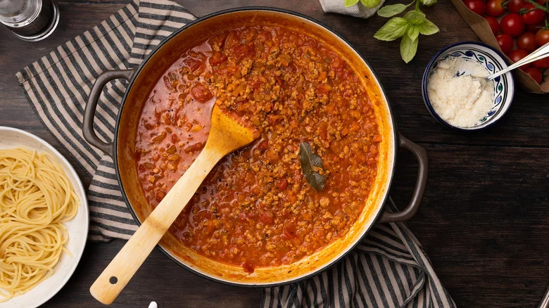 Turkey Bolognese in a cookware with spatula resting next to dishes of cheese and noodles